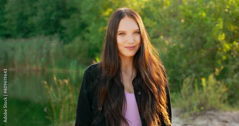 Portrait of a smiling young woman with long dark hair outdoors in a forest near a lake. Portrait of a smiling young woman with long dark hair outdoors in a forest near a lake.