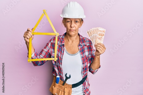 Middle age blonde woman holding building project and 50 lira banknotes skeptic and nervous, frowning upset because of problem. negative person. photo