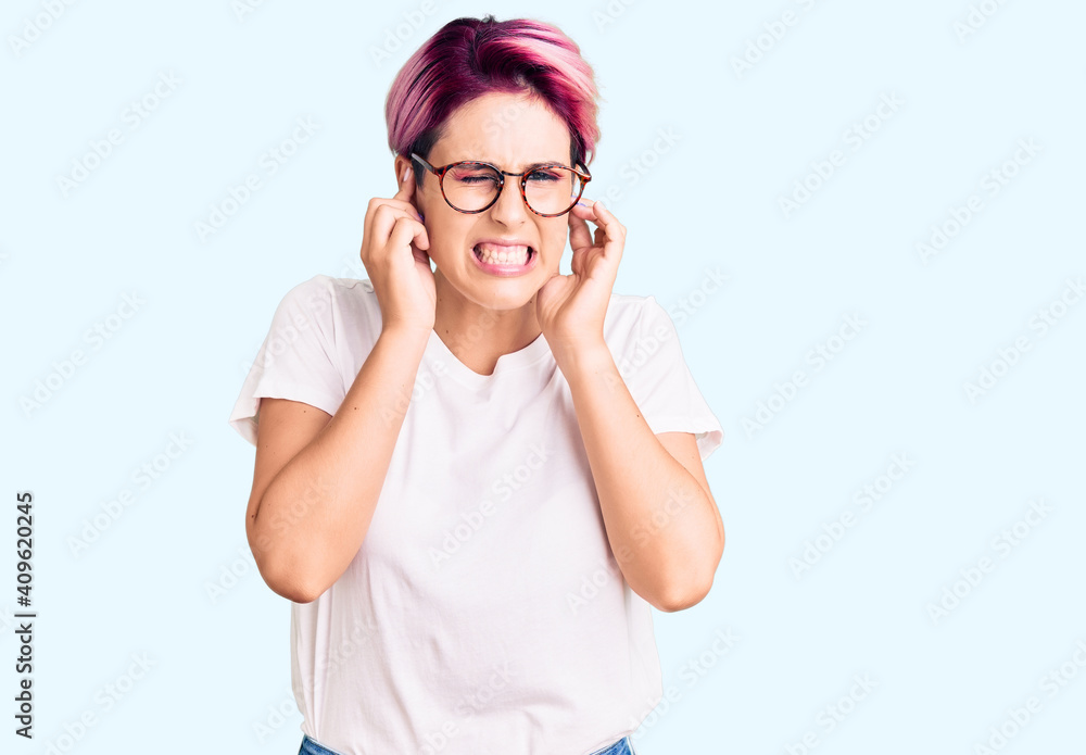 Young beautiful woman with pink hair wearing casual clothes and glasses covering ears with fingers with annoyed expression for the noise of loud music. deaf concept. Young beautiful woman with pink hair wearing casual clothes and glasses covering ears with fingers with annoyed expression for the noise of loud music. deaf concept.