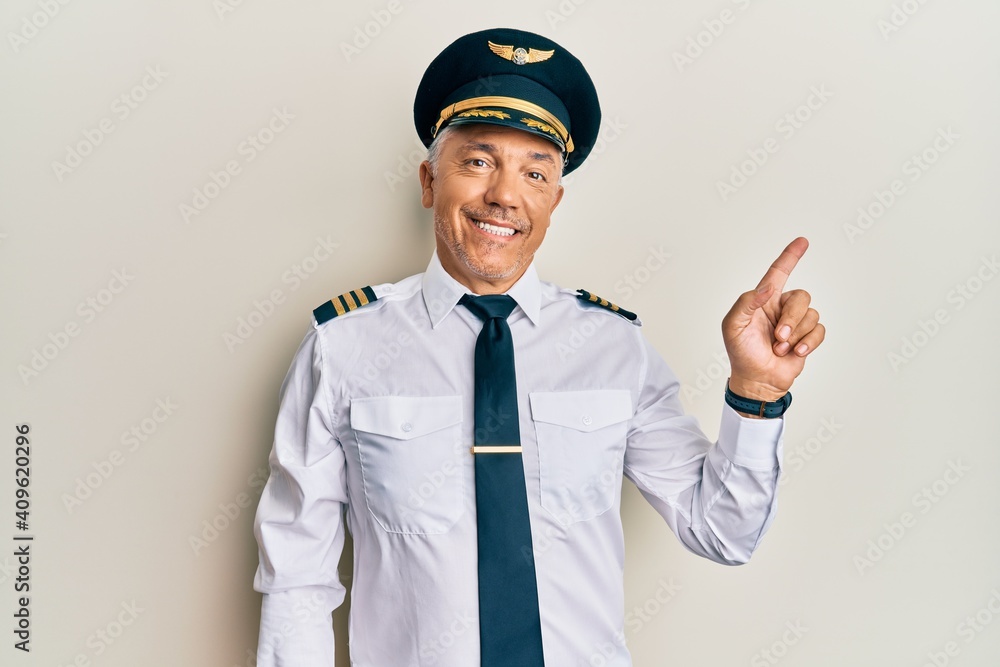 Handsome middle age mature man wearing airplane pilot uniform with a big smile on face, pointing with hand finger to the side looking at the camera. Handsome middle age mature man wearing airplane pilot uniform with a big smile on face, pointing with hand finger to the side looking at the camera.