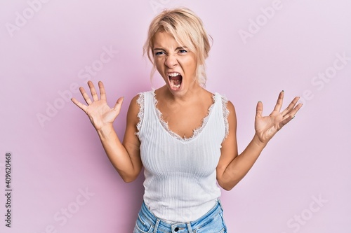 Young blonde girl wearing casual clothes crazy and mad shouting and yelling with aggressive expression and arms raised. frustration concept.