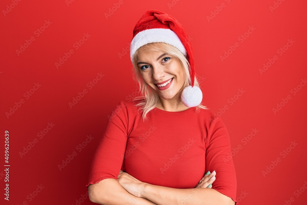 Young blonde girl wearing christmas hat happy face smiling with crossed arms looking at the camera. positive person. Young blonde girl wearing christmas hat happy face smiling with crossed arms looking at the camera. positive person.