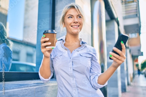 Free Download Young blonde woman smiling happy using smartphone and drinking take away coffee at the city. - GFXLoad