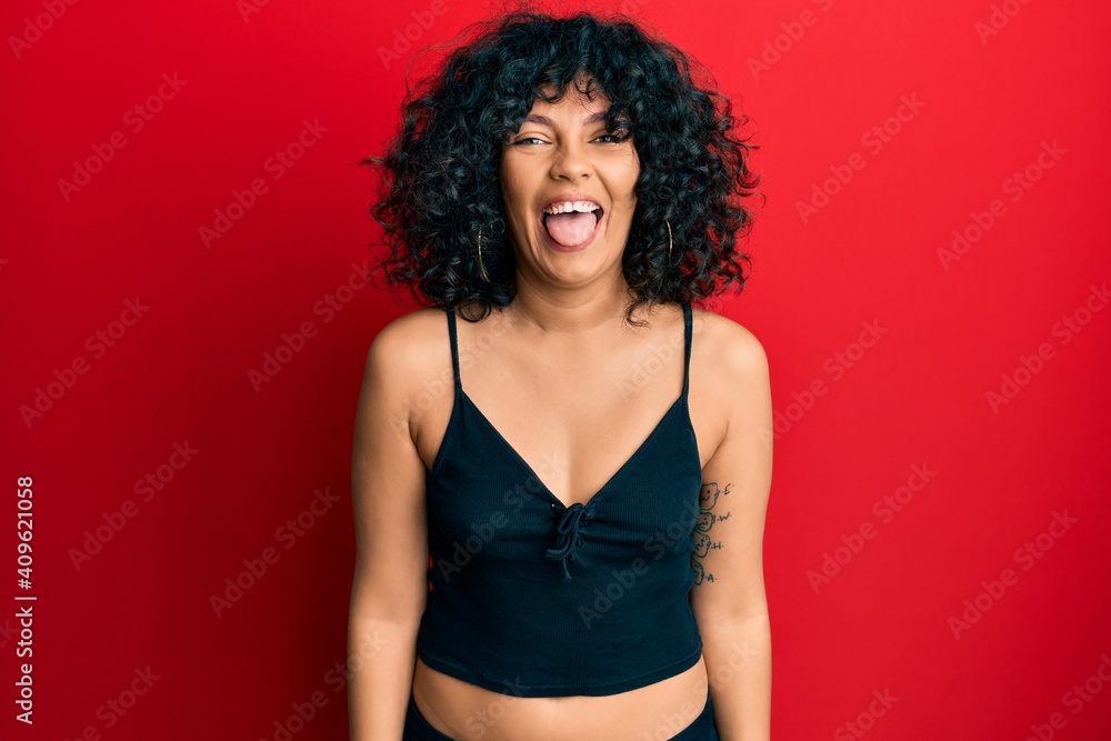 Young hispanic woman wearing casual style with sleeveless shirt sticking tongue out happy with funny expression. emotion concept. Young hispanic woman wearing casual style with sleeveless shirt sticking tongue out happy with funny expression. emotion concept.
