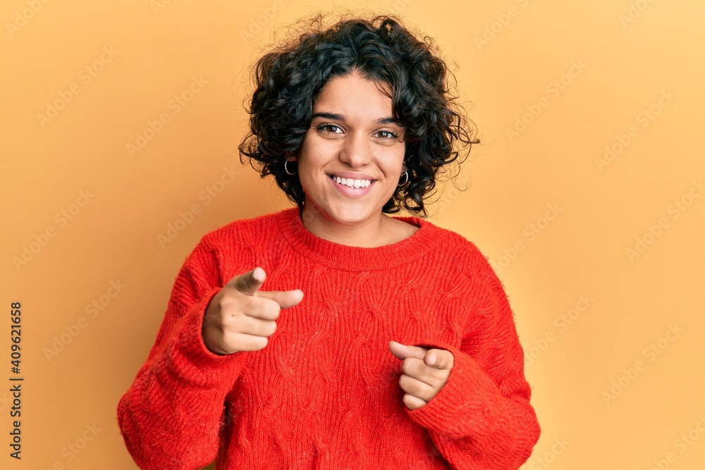 Young hispanic woman with curly hair wearing casual winter sweater pointing fingers to camera with happy and funny face. good energy and vibes. Young hispanic woman with curly hair wearing casual winter sweater pointing fingers to camera with happy and funny face. good energy and vibes.