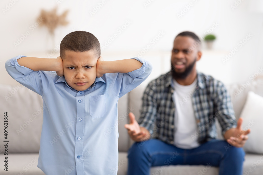Black Boy Covering Ears While Angry Father Shouting At Home Black Boy Covering Ears While Angry Father Shouting At Home