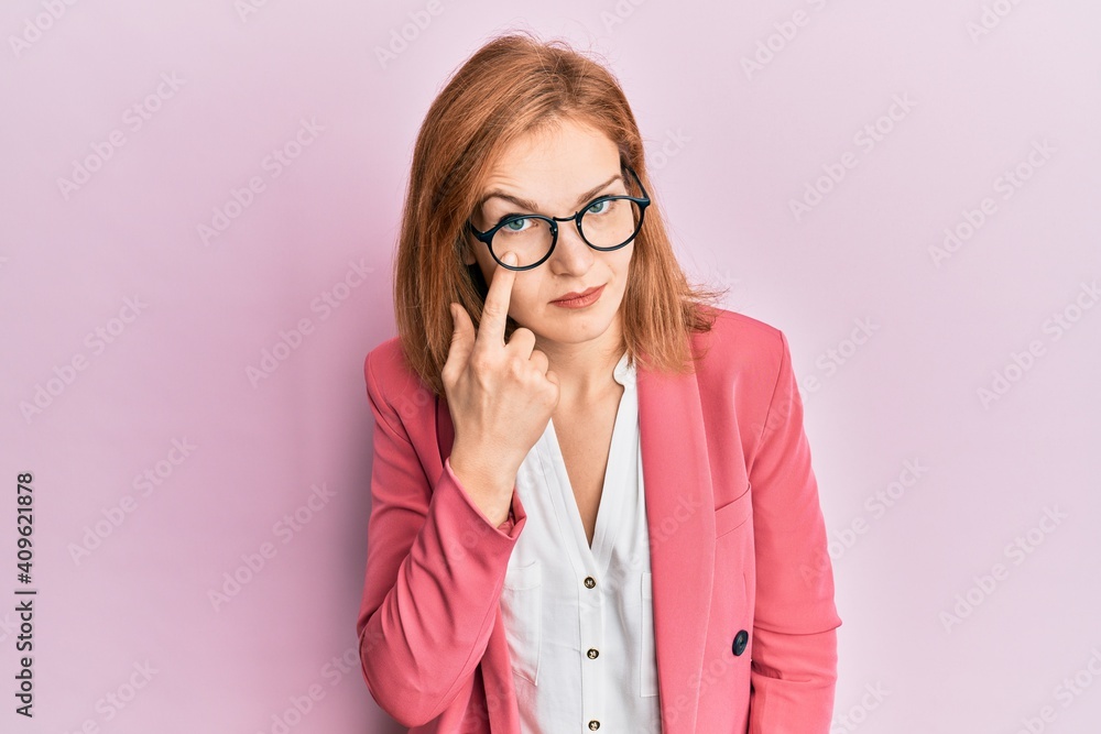 Young caucasian woman wearing business style and glasses pointing to the eye watching you gesture, suspicious expression