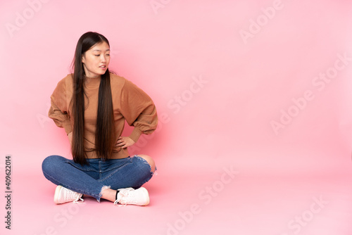 Young asian woman sitting on the floor isolated on pink background suffering from backache for having made an effort © luismolinero