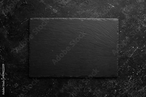 Black stone slate plate on a black stone background. Free copy space. Top view.
