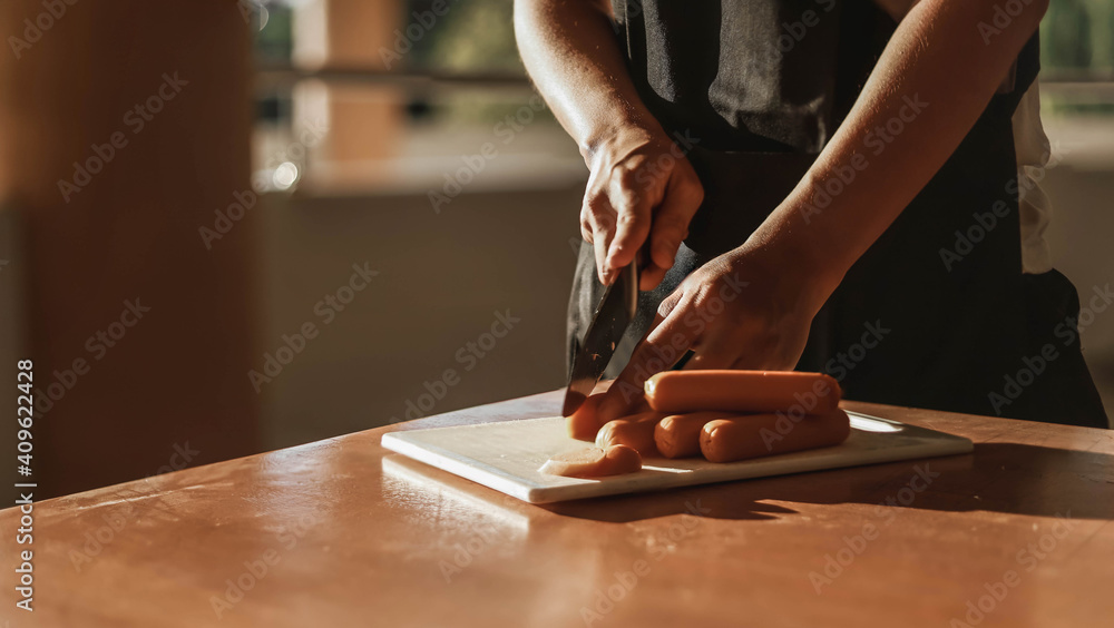 A man cutting sausages, he is cooking in the kitchen of his home, he spends time working from home in his own cooking practice, cooking ideas.