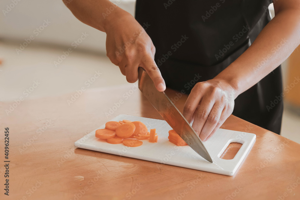A man cutting carrots, he is cooking in his home kitchen, he spends time working from home in his own cooking practice, cooking training ideas.