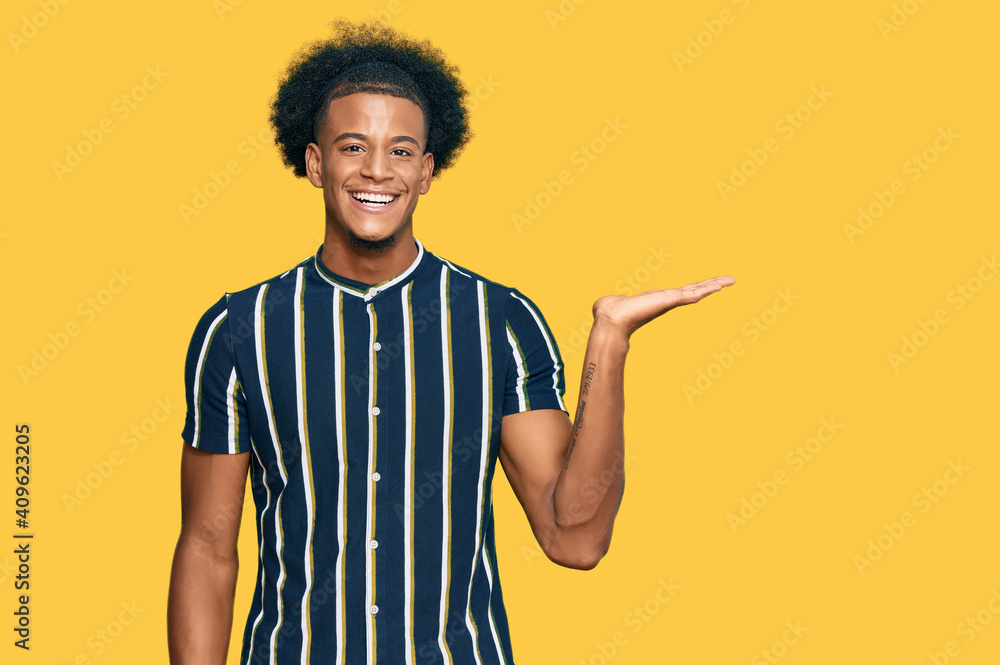 African american man with afro hair wearing casual clothes smiling cheerful presenting and pointing with palm of hand looking at the camera. African american man with afro hair wearing casual clothes smiling cheerful presenting and pointing with palm of hand looking at the camera.