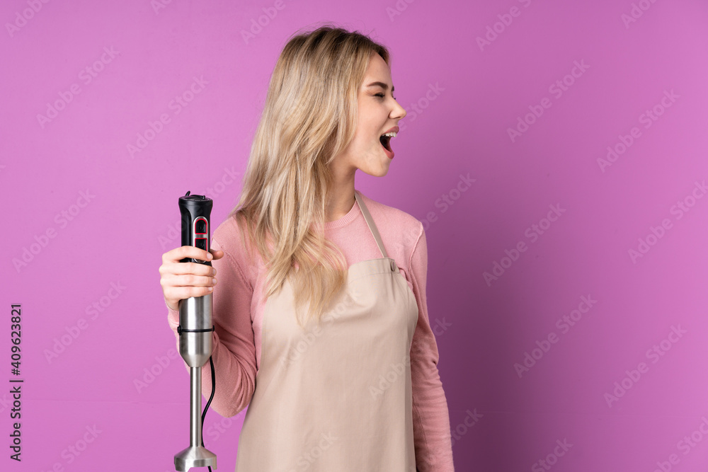 Teenager Russian girl using hand blender isolated on purple background laughing in lateral position Teenager Russian girl using hand blender isolated on purple background laughing in lateral position