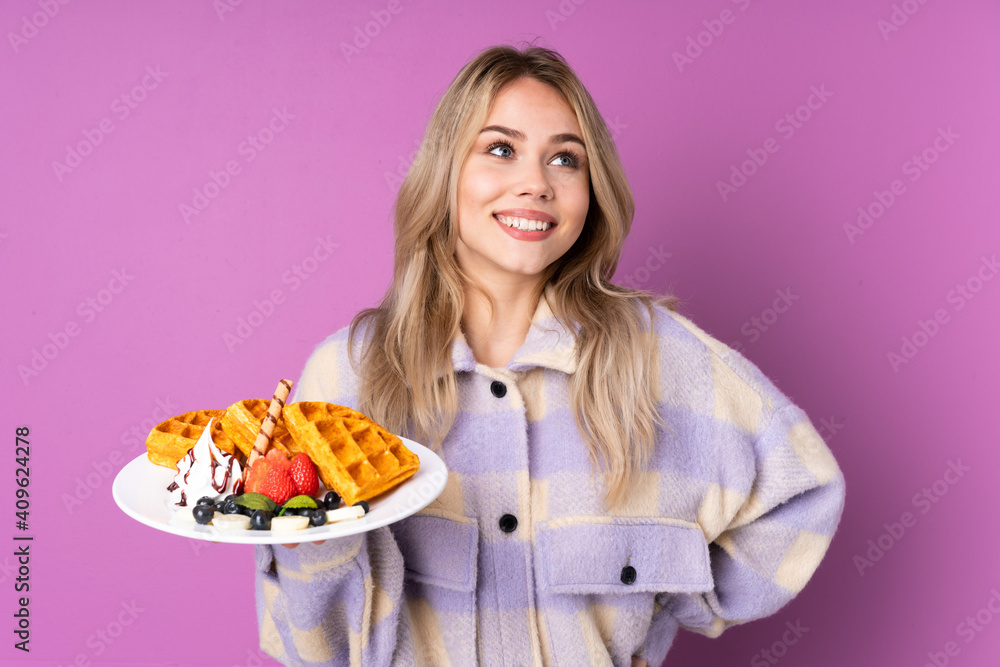 Teenager Russian girl holding waffles isolated on purple background posing with arms at hip and smiling Teenager Russian girl holding waffles isolated on purple background posing with arms at hip and smiling