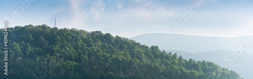 Panorama. Na pierwszym planie góra porośnięta lasem z wieżą na szczycie, w tle pasmo gór.