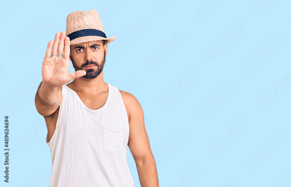 Young hispanic man wearing casual summer hat doing stop sing with palm of the hand. warning expression with negative and serious gesture on the face. Young hispanic man wearing casual summer hat doing stop sing with palm of the hand. warning expression with negative and serious gesture on the face.