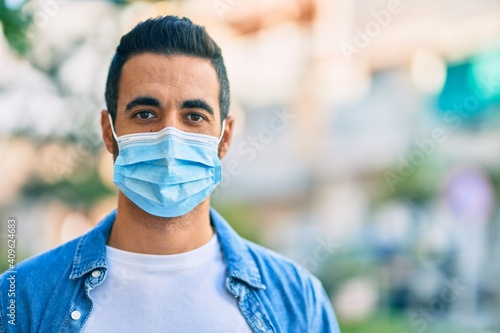 Young hispanic man wearing medical mask standing at the city.