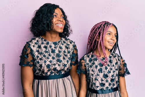 Beautiful african american mother and daughter wearing sexy party dress looking away to side with smile on face, natural expression. laughing confident. photo