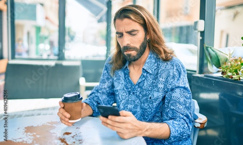 Photos Young middle eastern man with sad face using smartphone and drinking coffee at coffee shop
