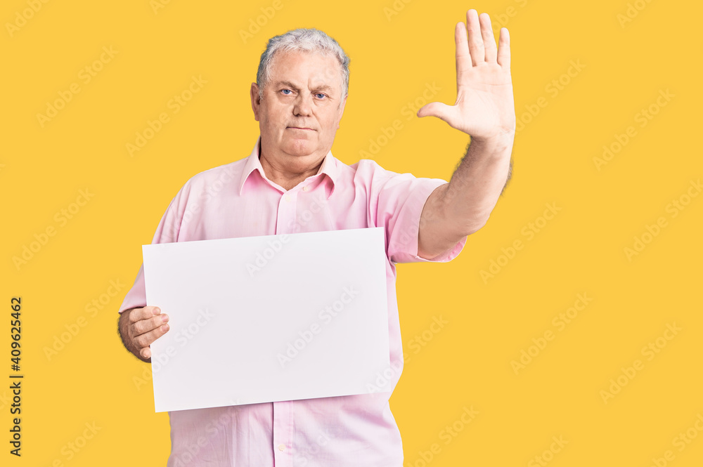 Senior grey-haired man holding blank empty banner with open hand doing stop sign with serious and confident expression, defense gesture Senior grey-haired man holding blank empty banner with open hand doing stop sign with serious and confident expression, defense gesture