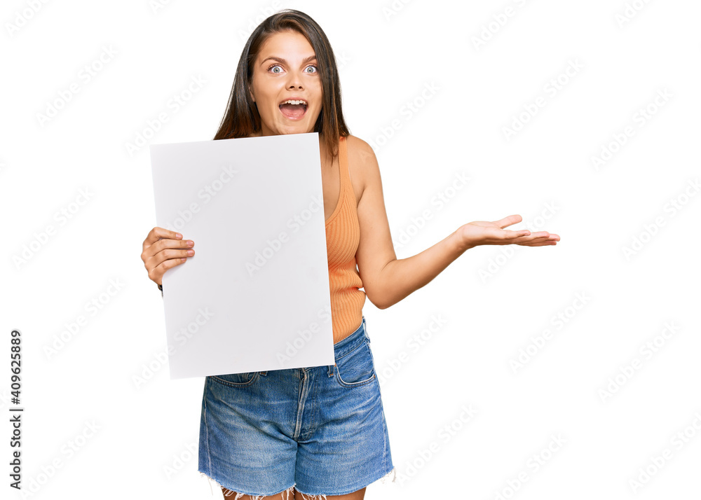 Young caucasian woman holding blank empty banner celebrating victory with happy smile and winner expression with raised hands Young caucasian woman holding blank empty banner celebrating victory with happy smile and winner expression with raised hands