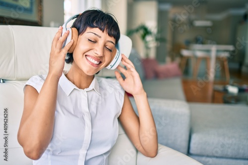 Beautiful brunette woman with short hair at home listening to music wearing headphones