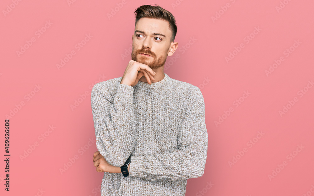 Young redhead man wearing casual winter sweater with hand on chin thinking about question, pensive expression. smiling with thoughtful face. doubt concept. Young redhead man wearing casual winter sweater with hand on chin thinking about question, pensive expression. smiling with thoughtful face. doubt concept.