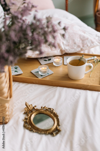 Cup of tea on a tray with candles on a bed with a mirror and dried flowers