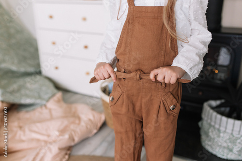 Girl child ties a belt in a brown overalls