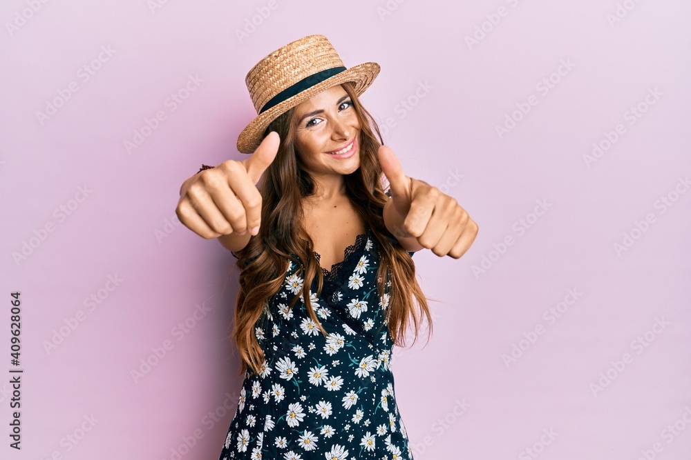 Young brunette woman wearing summer hat approving doing positive gesture with hand, thumbs up smiling and happy for success. winner gesture. Young brunette woman wearing summer hat approving doing positive gesture with hand, thumbs up smiling and happy for success. winner gesture.