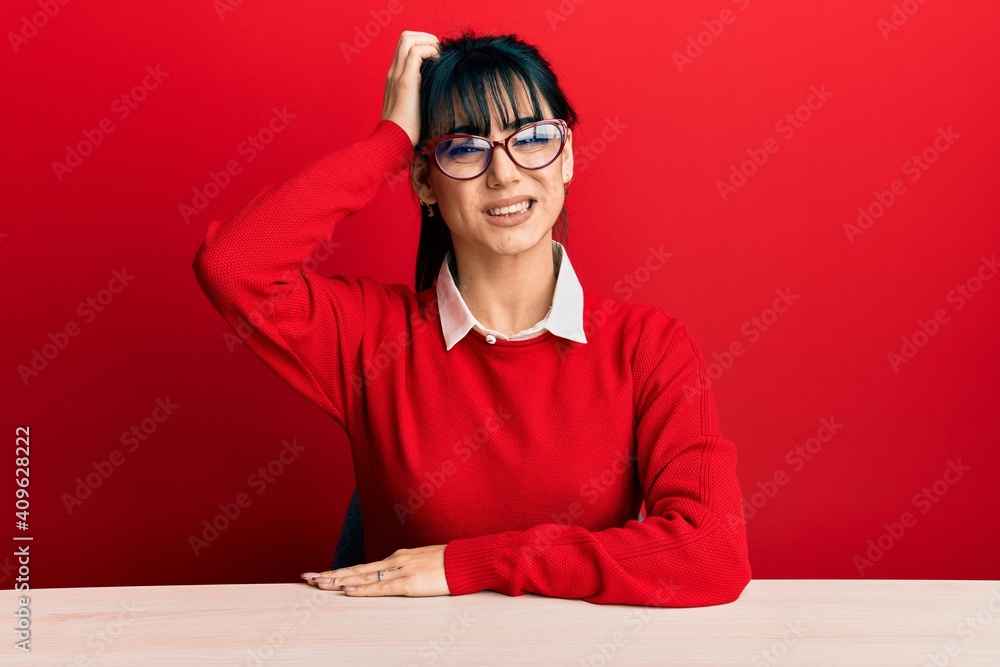Young brunette woman with bangs wearing glasses sitting on the table confuse and wonder about question. uncertain with doubt, thinking with hand on head. pensive concept. Young brunette woman with bangs wearing glasses sitting on the table confuse and wonder about question. uncertain with doubt, thinking with hand on head. pensive concept.