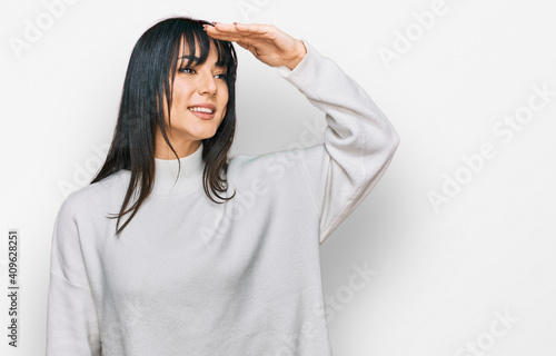 Young brunette woman with bangs wearing casual turtleneck sweater very happy and smiling looking far away with hand over head. searching concept.