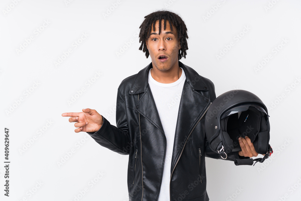 Young african american man holding a motorcycle helmet isolated on white background surprised and pointing side Young african american man holding a motorcycle helmet isolated on white background surprised and pointing side