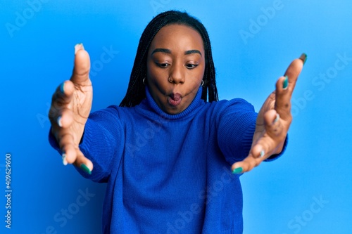 Young african american woman with arms stretched hug gesture making fish face with mouth and squinting eyes, crazy and comical.