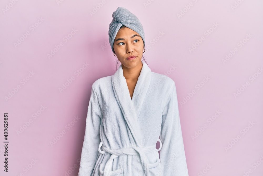Young chinese woman wearing shower towel cap and bathrobe smiling looking to the side and staring away thinking. Young chinese woman wearing shower towel cap and bathrobe smiling looking to the side and staring away thinking.