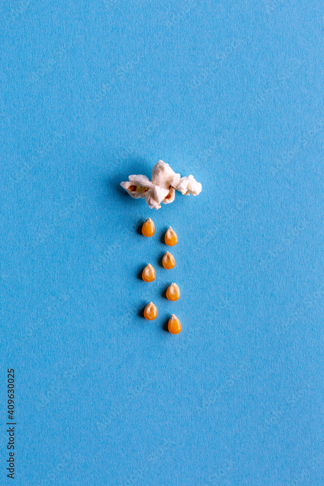 Small popcorn cloud with rain made out of corn kernels on blue background Small popcorn cloud with rain made out of corn kernels on blue background