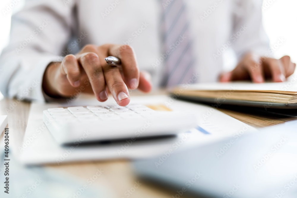 A business man uses a calculator to check monthly sales of a salesperson from a sales summary document in a bar graph format. Sales management concept. A business man uses a calculator to check monthly sales of a salesperson from a sales summary document in a bar graph format. Sales management concept.