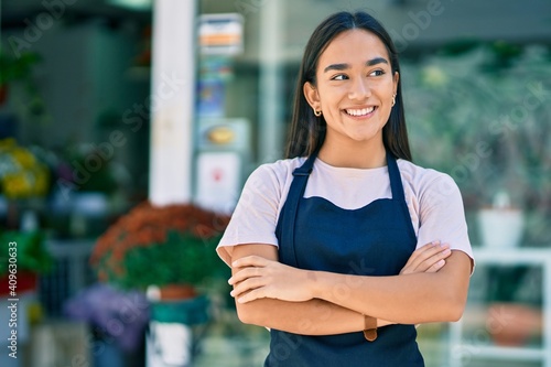 Young latin shopkeeper girl with arms crossed smiling happy standing at the florist