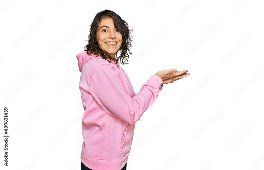Young hispanic woman wearing casual sweatshirt pointing aside with hands open palms showing copy space, presenting advertisement smiling excited happy Young hispanic woman wearing casual sweatshirt pointing aside with hands open palms showing copy space, presenting advertisement smiling excited happy