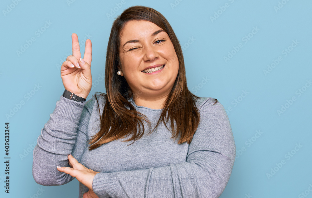 Beautiful brunette plus size woman wearing casual clothes smiling with happy face winking at the camera doing victory sign with fingers. number two. Beautiful brunette plus size woman wearing casual clothes smiling with happy face winking at the camera doing victory sign with fingers. number two.