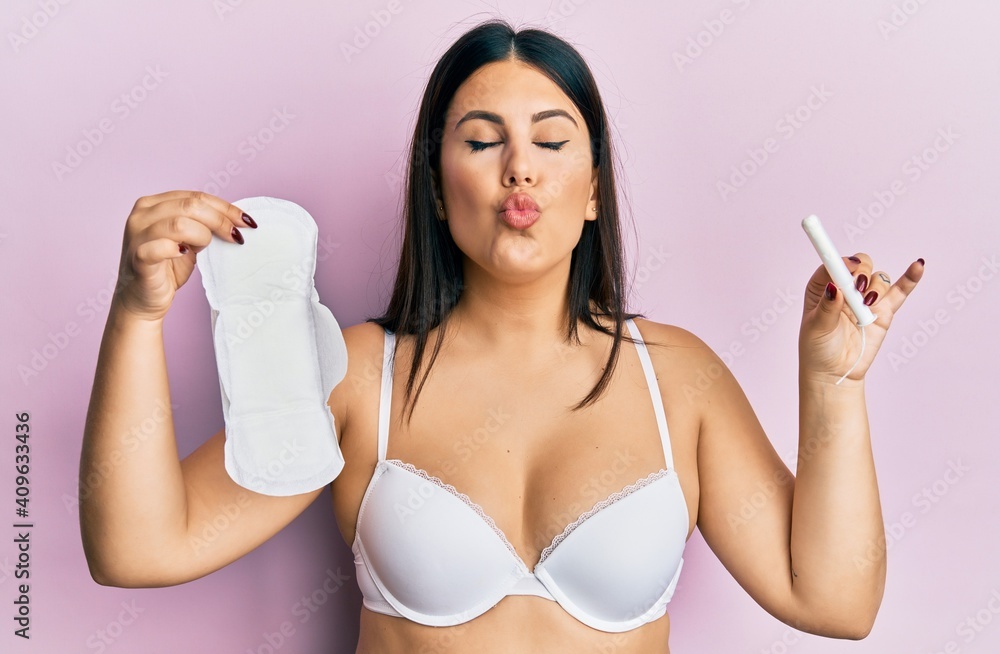 Beautiful brunette woman holding sanitary pad and cotton tampon looking at the camera blowing a kiss being lovely and sexy. love expression. Beautiful brunette woman holding sanitary pad and cotton tampon looking at the camera blowing a kiss being lovely and sexy. love expression.