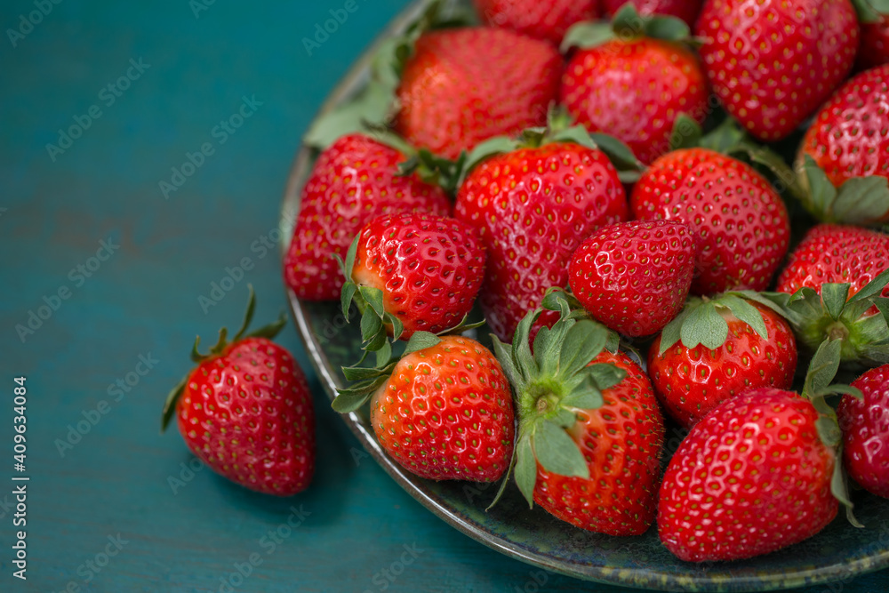 Ripe strawberries in a plate close-up on a blue-green background