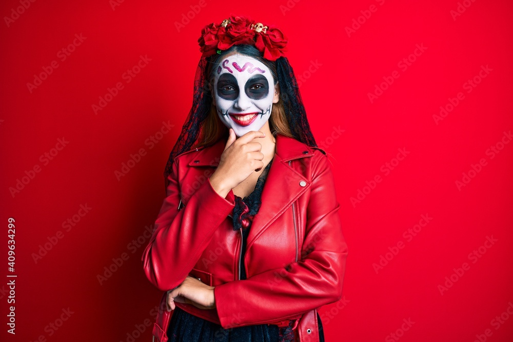 Woman wearing day of the dead costume over red looking confident at the camera smiling with crossed arms and hand raised on chin. thinking positive. Woman wearing day of the dead costume over red looking confident at the camera smiling with crossed arms and hand raised on chin. thinking positive.
