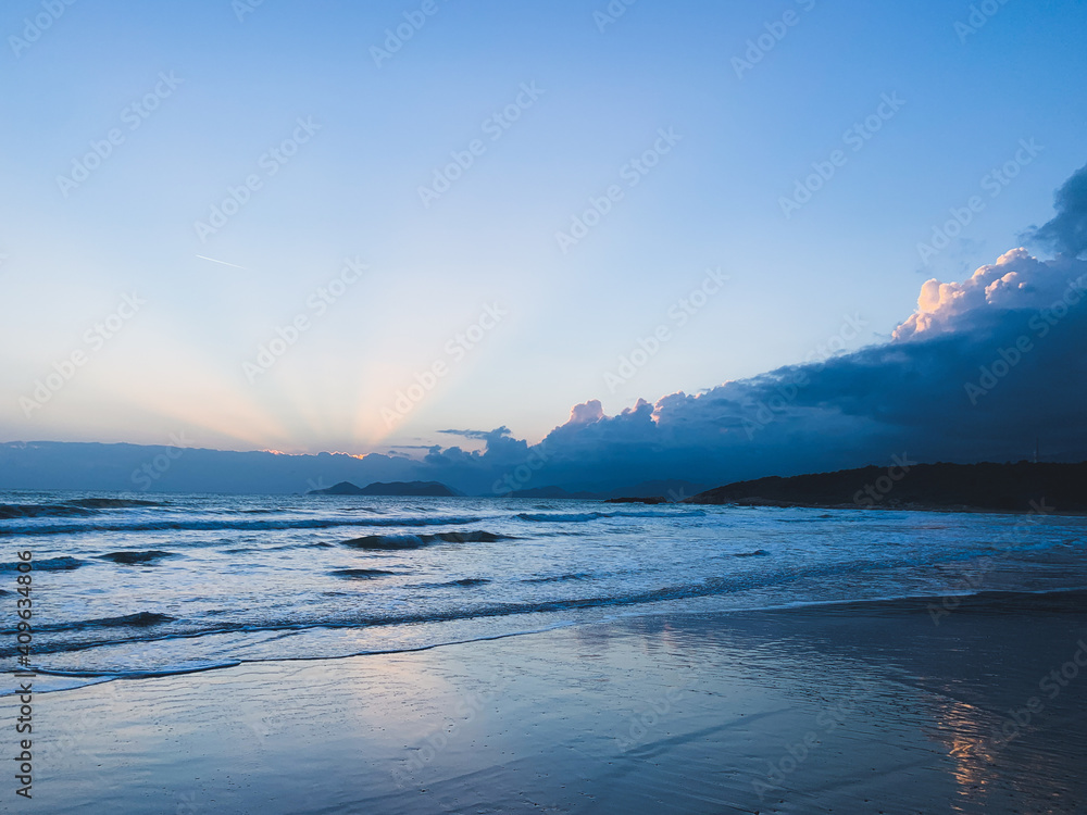 Orange sunrays shining from the clouds at the evening sea, sand beach, clear sky