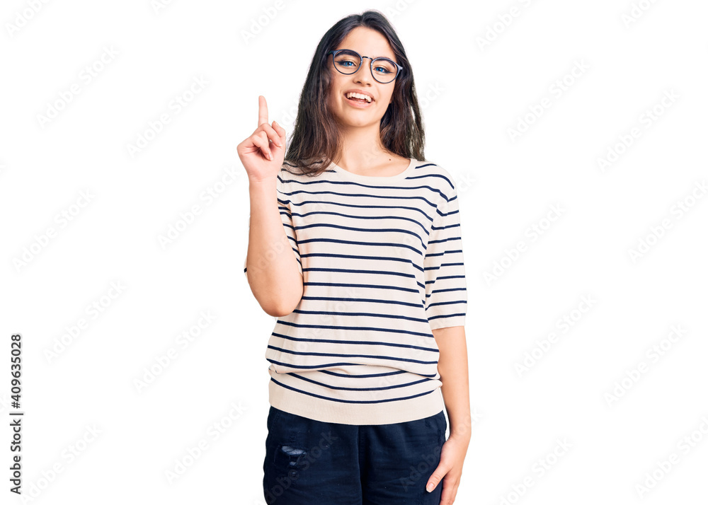 Brunette teenager girl wearing casual clothes and glasses showing and pointing up with finger number one while smiling confident and happy. Brunette teenager girl wearing casual clothes and glasses showing and pointing up with finger number one while smiling confident and happy.