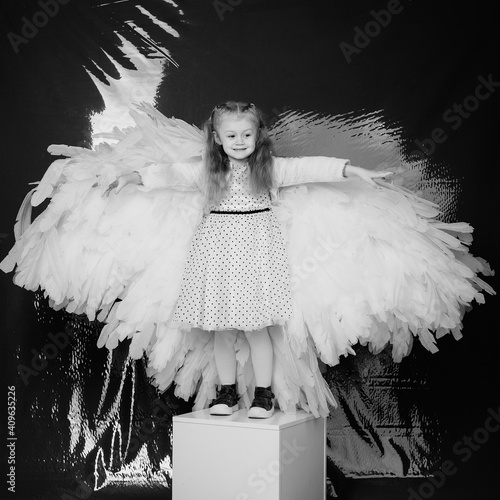 little girl 4 years old in white angel wings on a red latex background in the studio for valentine's day