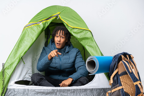 Young african american man inside a camping green tent surprised and pointing front