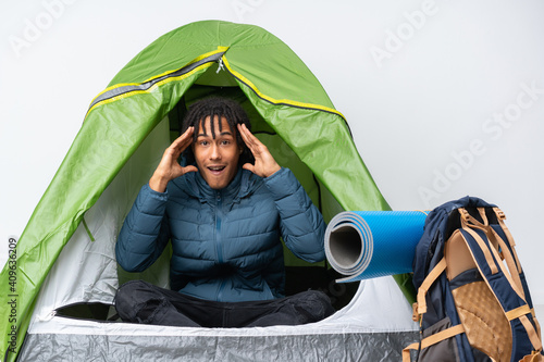 Young african american man inside a camping green tent with surprise expression