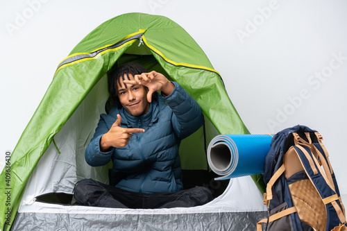 Young african american man inside a camping green tent focusing face. Framing symbol