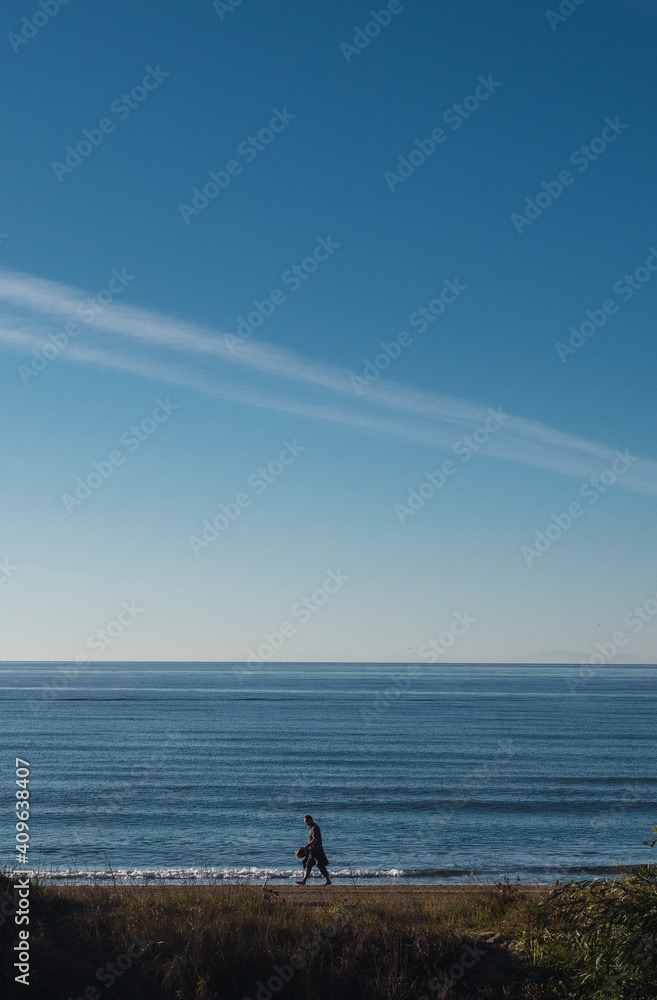 Unreconognizable person silhouette walking on the beach. Mediterranean sea and blue sky